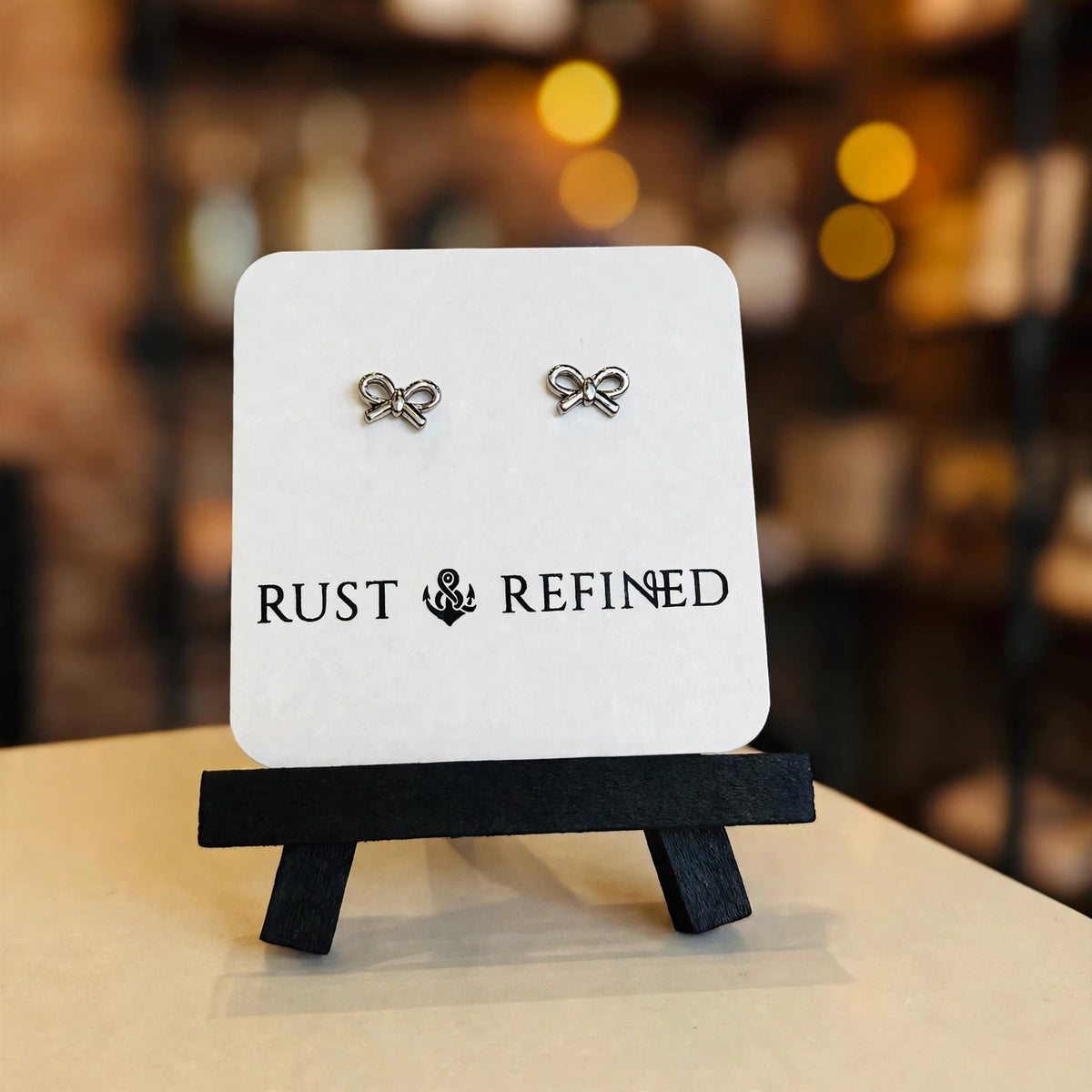 Silver bow stud earrings on a Rust & Refined card