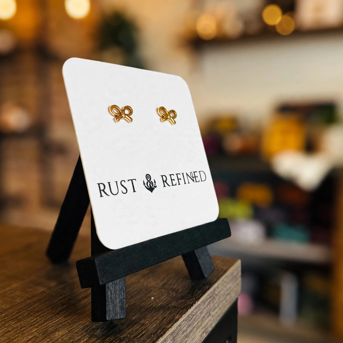 Gold bow stud earrings on a Rust & Refined card, angled view