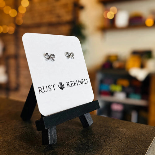 Silver bow stud earrings on a Rust & Refined card, angled view