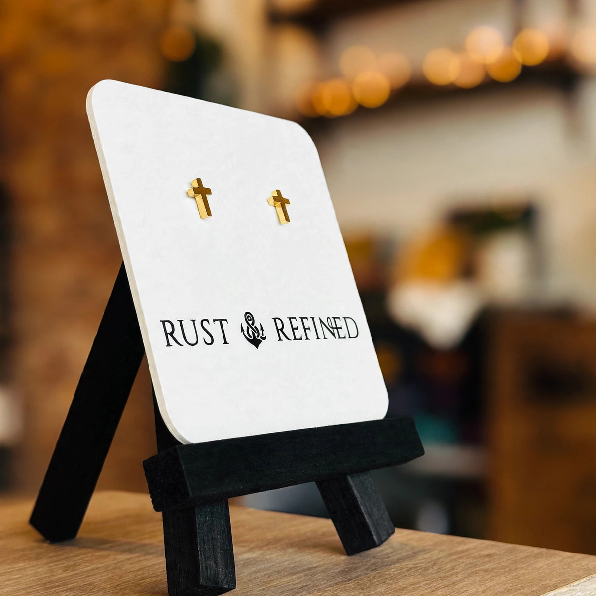 Gold cross stud earrings on a Rust & Refined card, angled view
