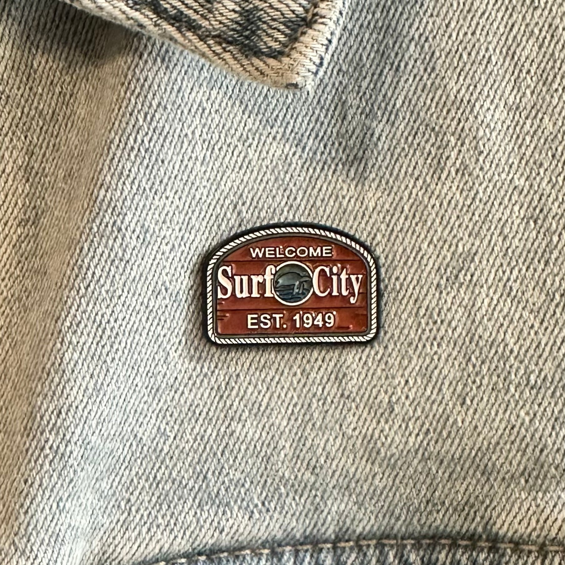 Denim jacket with 'Welcome to Surf City' patch on a close-up of fabric.