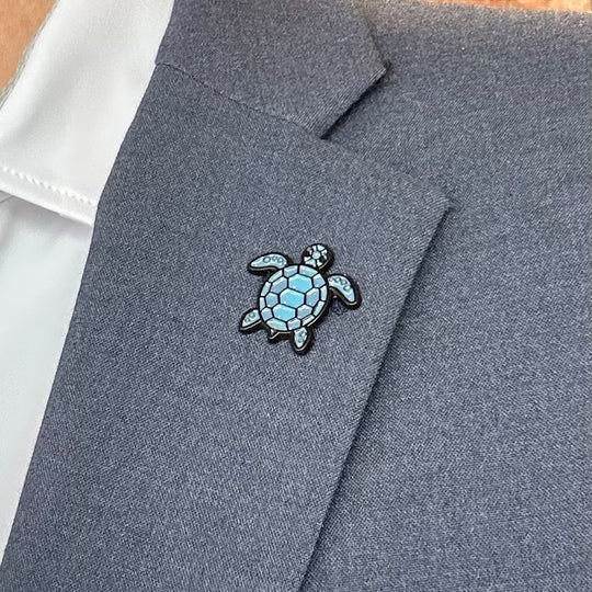 Gray blazer with a turtle pin on a white shirt against a brick wall background