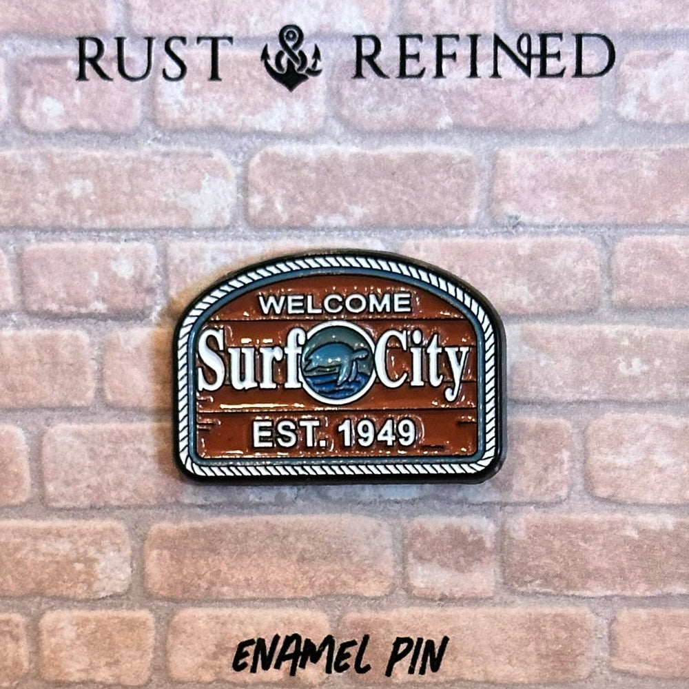 Enamel pin with 'Surf City' design on a brick background, featuring the brand 'Rust & Refined'.