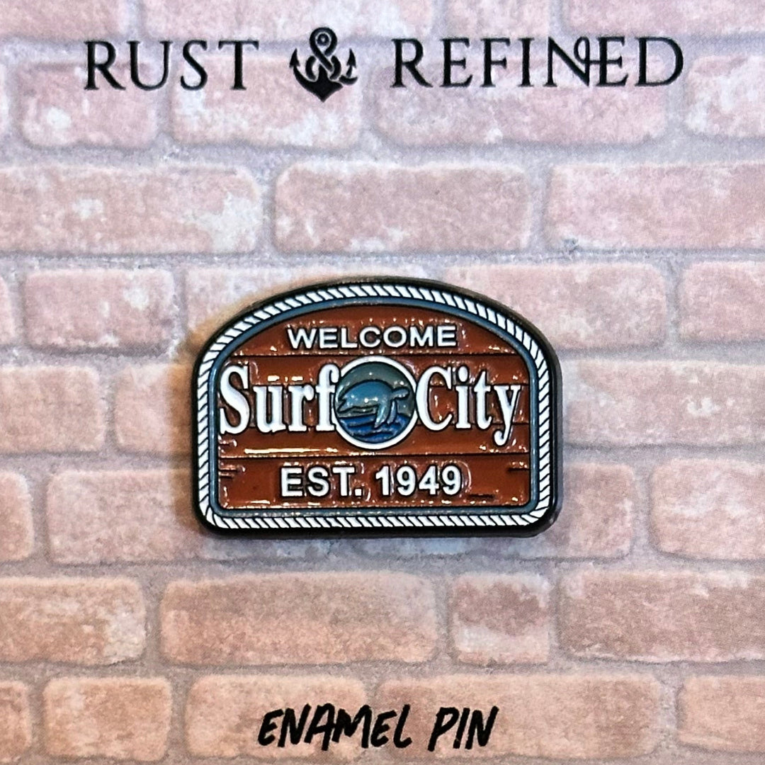 Enamel pin with 'Surf City' design on a brick background, featuring the brand 'Rust & Refined'.