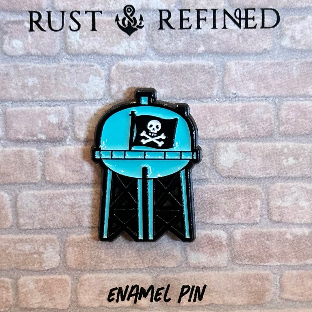 Enamel pin of a water tower with a pirate flag on a 'Rust & Refined' branded card.