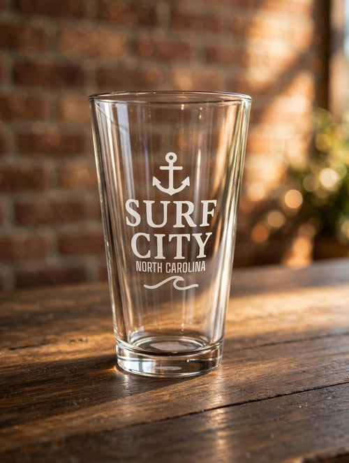 Surf City Anchor pint glass on a dark wood counter, brick wall behind