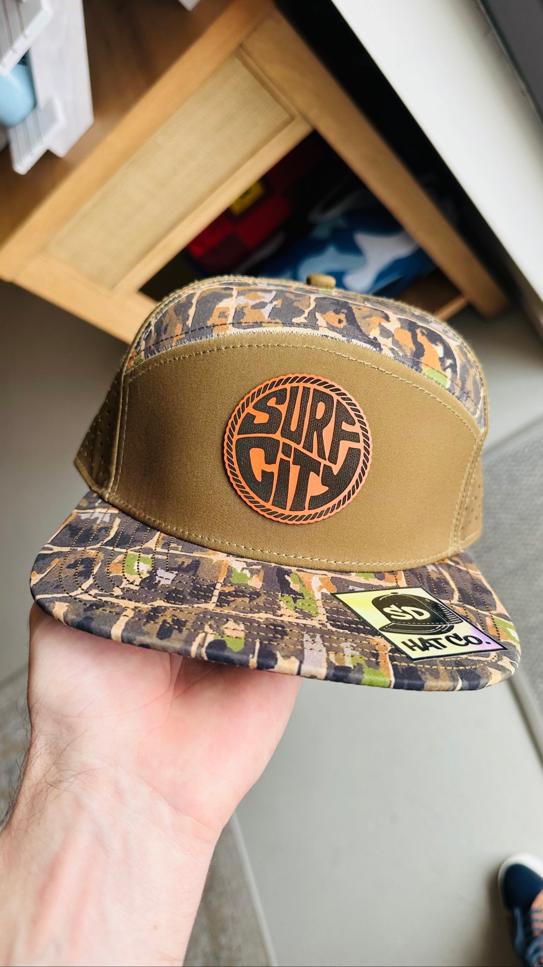 Tan and dark camo trucker hat with Surf City leather circle patch