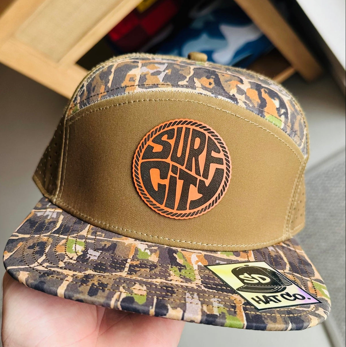Tan and dark camo trucker hat with Surf City leather circle patch